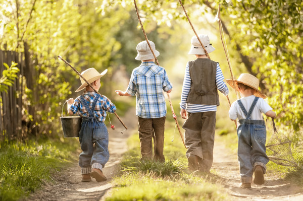 Four boys with fishing rods go on a fishing trip on the narrow rural road in sunny summer day