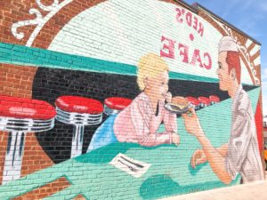 Mural in downtown Sevierville showing a young Dolly Parton getting served a hamburger at Red's Café. 