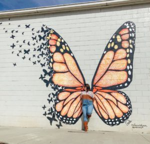 Young woman standing in front of mural of monarch butterfly wings 