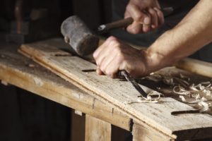 Image of someone shaving a layer of wood with a hammer and a chisel-like tool. 